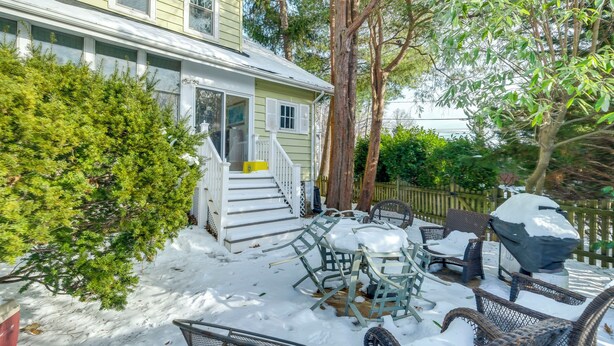 Una casa de dos pisos con un porche, mobiliario exterior y un patio cubierto de nieve.
