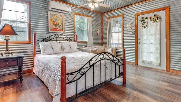 A bedroom with a metal-framed bed, wooden floor, and a ceiling fan. - Cozy Couple's Cottage w/ View Near Canyon Lake! (Canyon Lake)