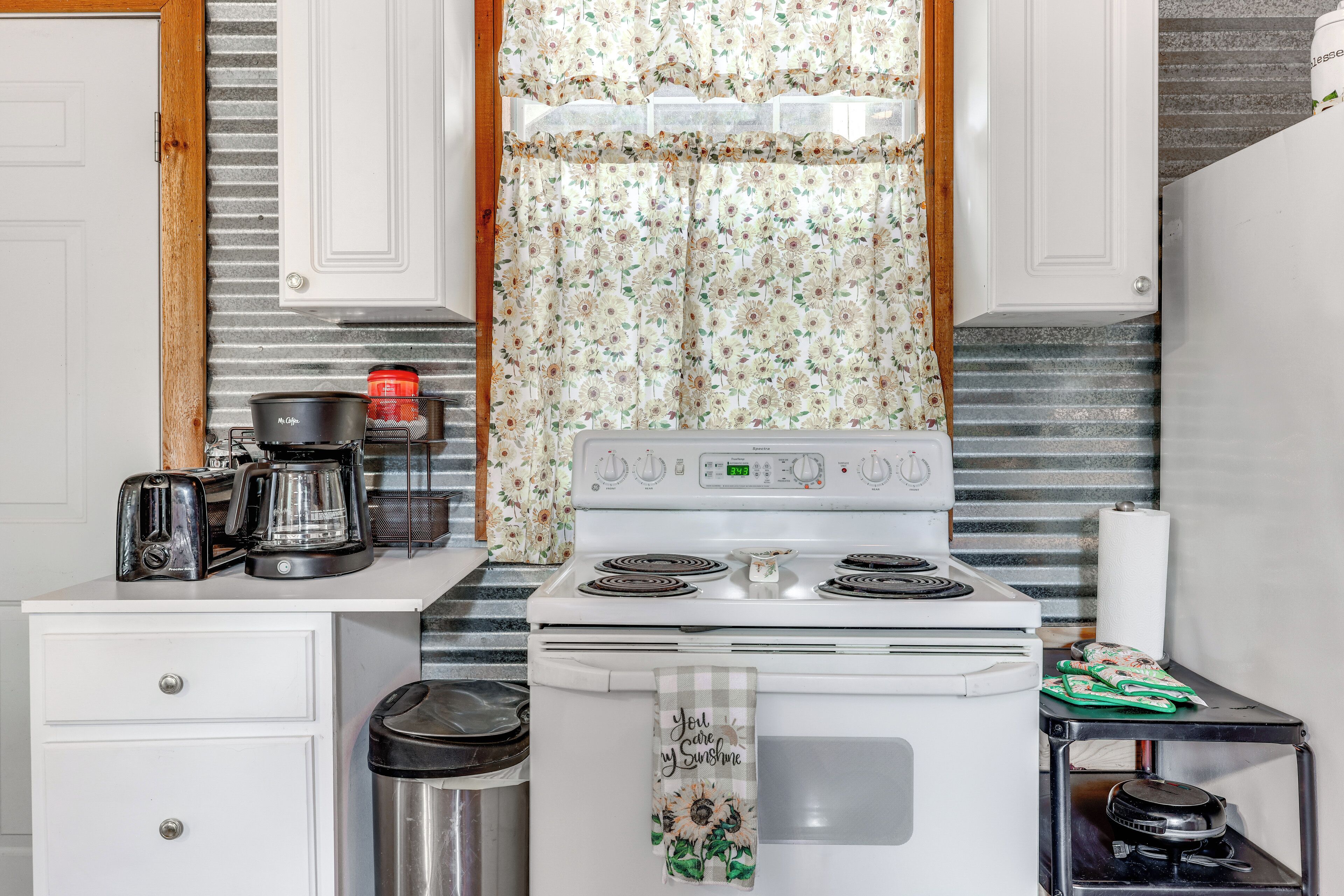 A kitchen with a stove, a coffee maker, and a trash can.
