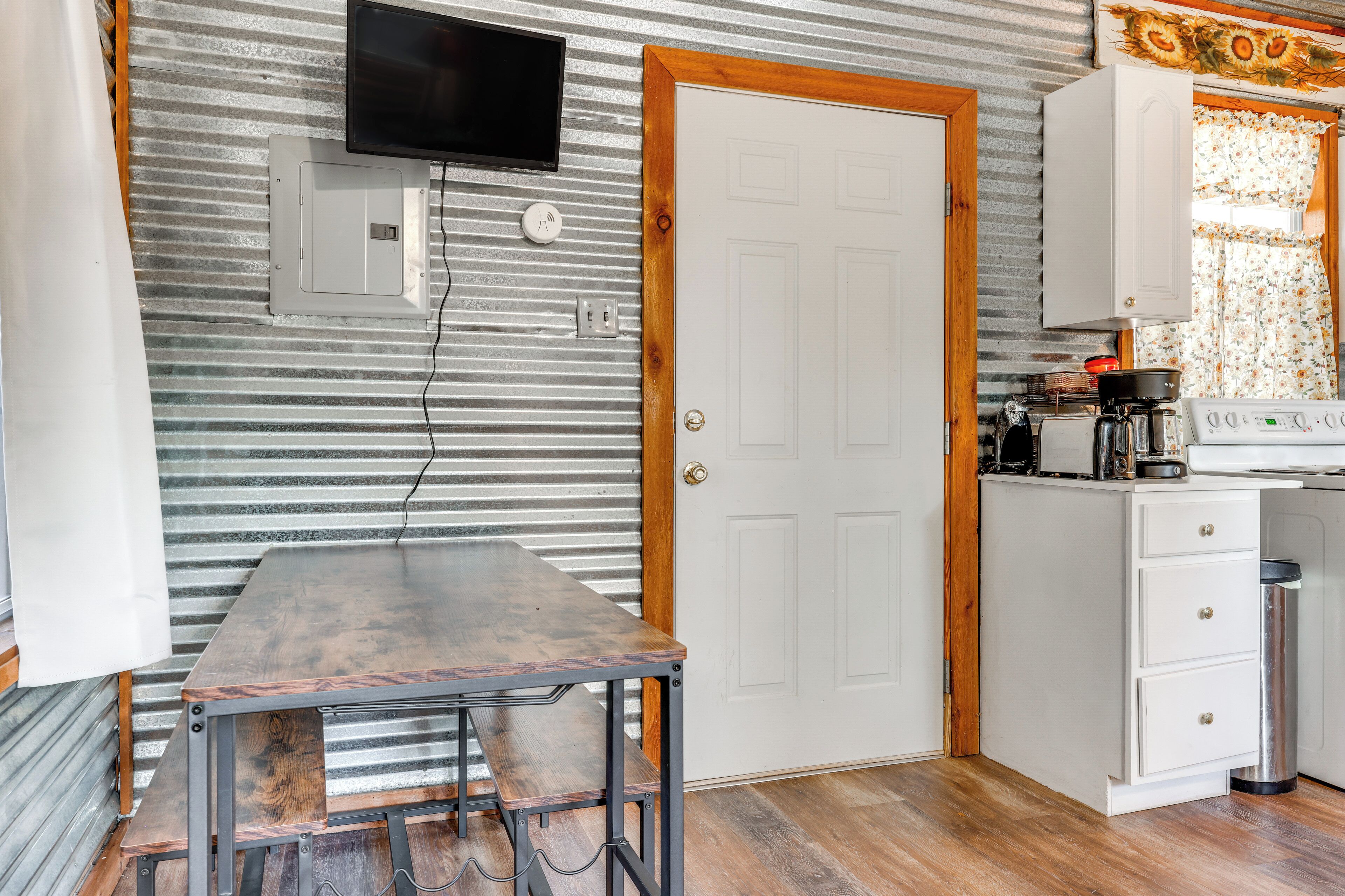 Une cuisine de taille réduite, avec une table en bois, un meuble blanc et un téléviseur fixé au mur.