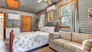 A rustic bedroom with a bed, a sofa, a wooden floor, and a kitchen area with a window. - Cozy Couple's Cottage w/ View Near Canyon Lake! (Canyon Lake)