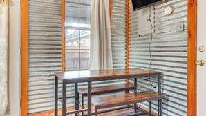 A room with a wooden table, a window with a curtain, a television mounted on the wall, and a power outlet. - Cozy Couple's Cottage w/ View Near Canyon Lake! (Canyon Lake)