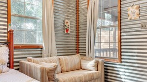 A cozy room with a striped couch, a wooden headboard, and a large window with curtains. - Cozy Couple's Cottage w/ View Near Canyon Lake! (Canyon Lake)
