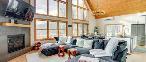 A spacious living room with a large sectional sofa, a fireplace, and a kitchen in the background.