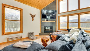 Una sala de estar acogedora con chimenea, ventanas amplias, un banco y un perro descansando en un sofá.