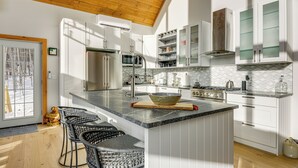 Una cocina moderna con armarios blancos, una isla grande con taburetes de bar y un techo de madera.