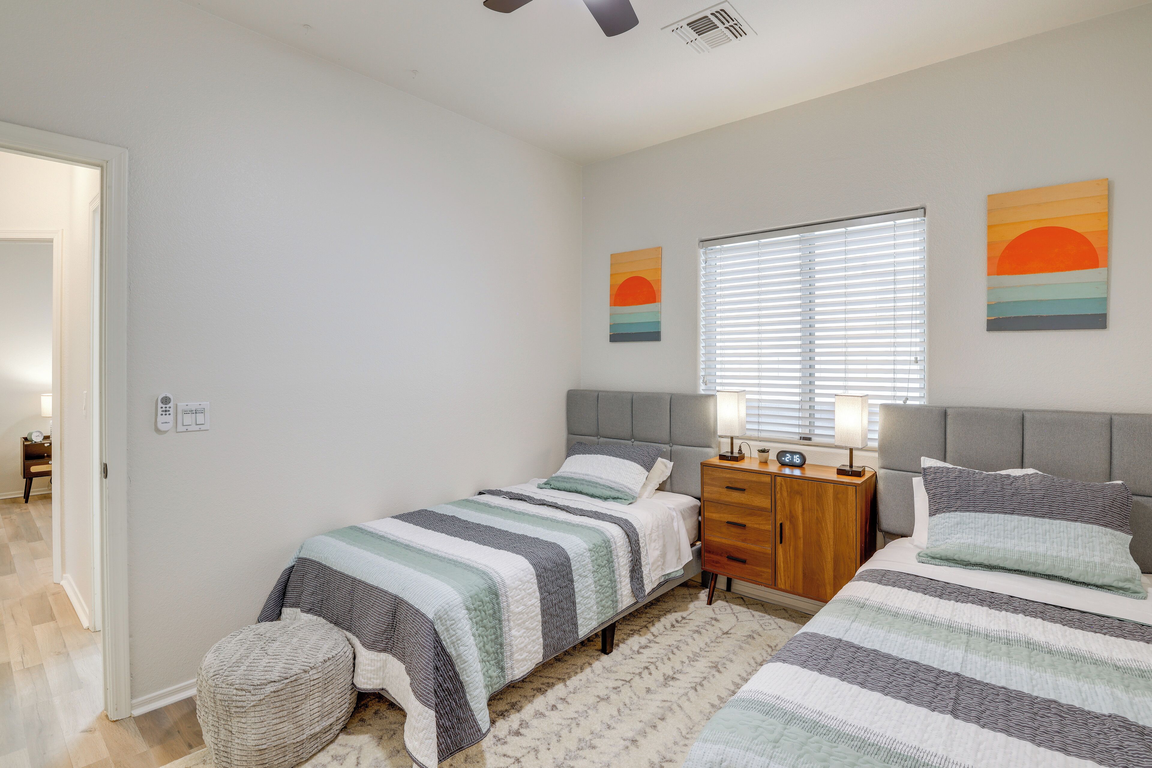 A bedroom with two single beds, a wooden nightstand, a bedside table with lamps, and a window with blinds.
