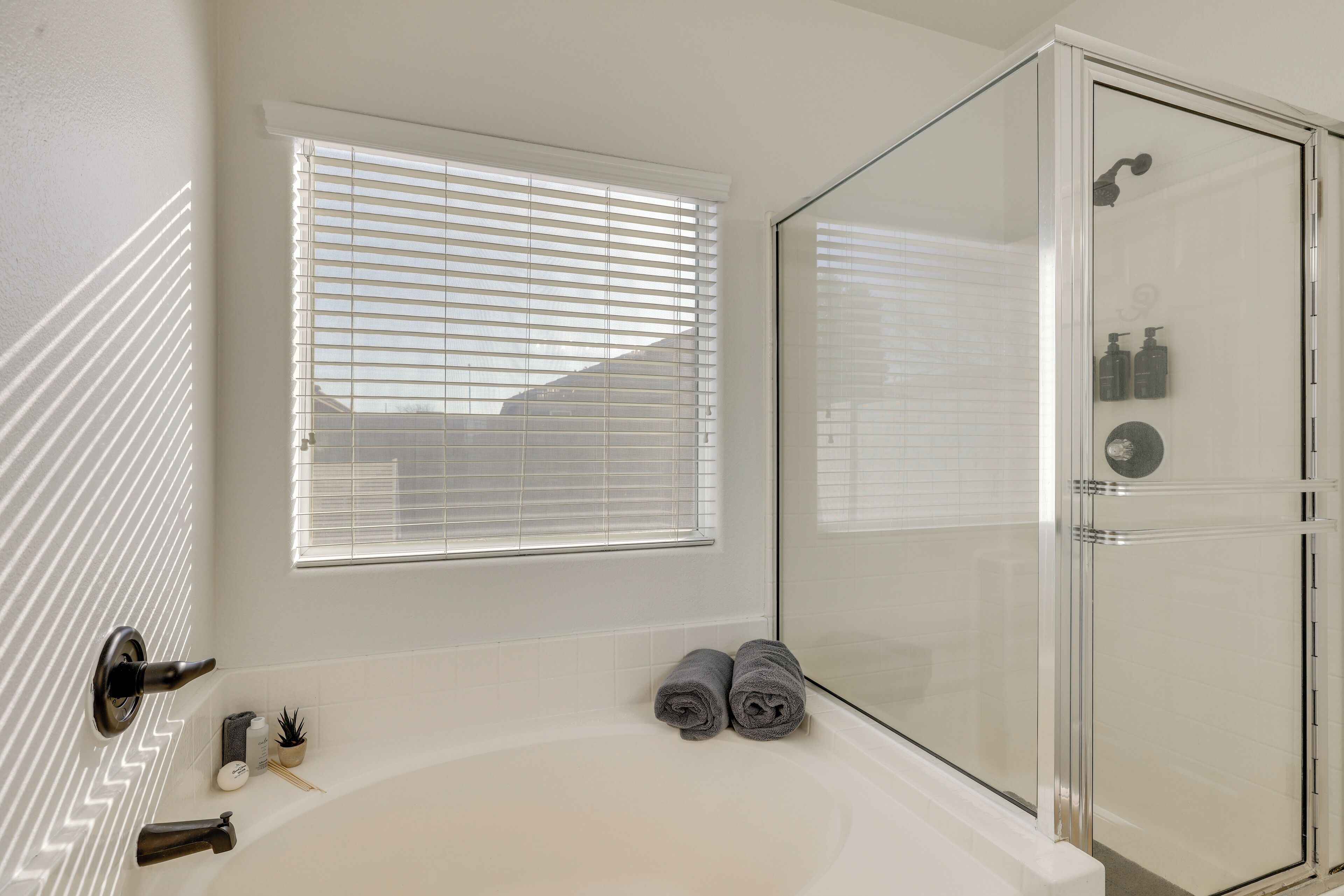 A bathroom with a glass-enclosed shower, a bathtub, and a window with blinds.