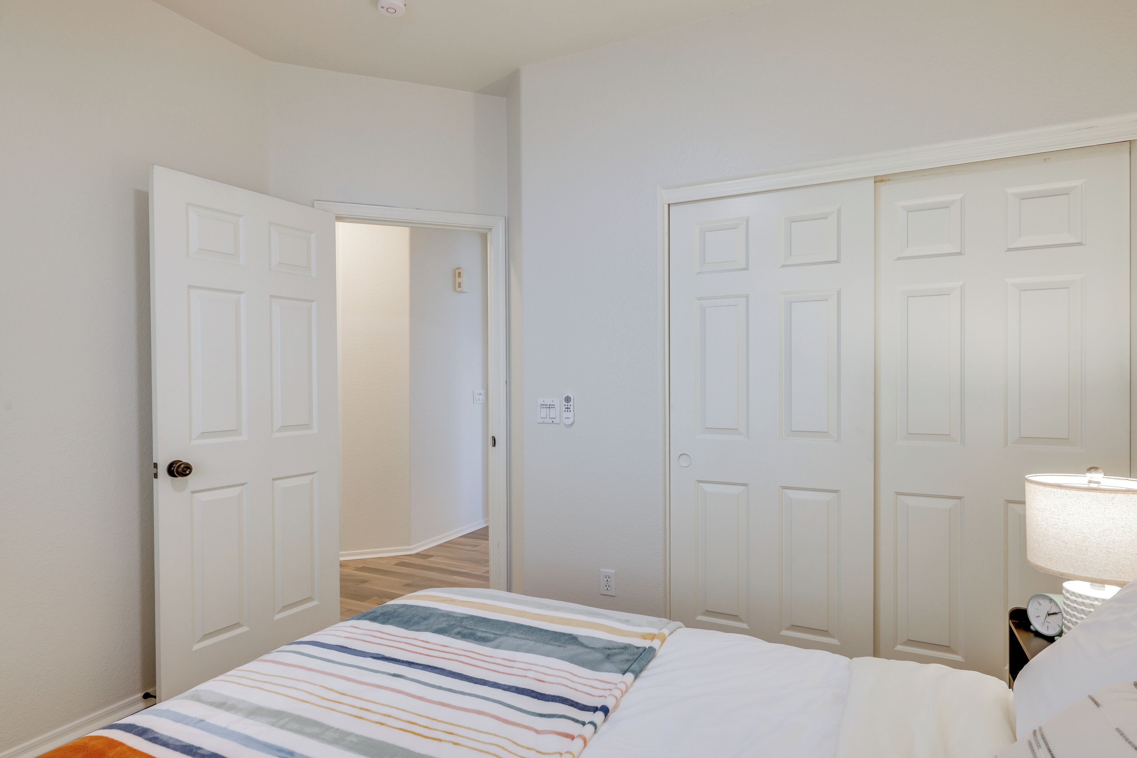 A bedroom with a bed, a nightstand with a lamp, and two doors leading to other rooms.