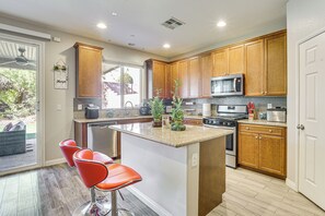 A modern kitchen with wooden cabinets, a central island, and a microwave. - 1 Mi to Aliante Casino: Townhome w/ Fenced Yard! (North Las Vegas)