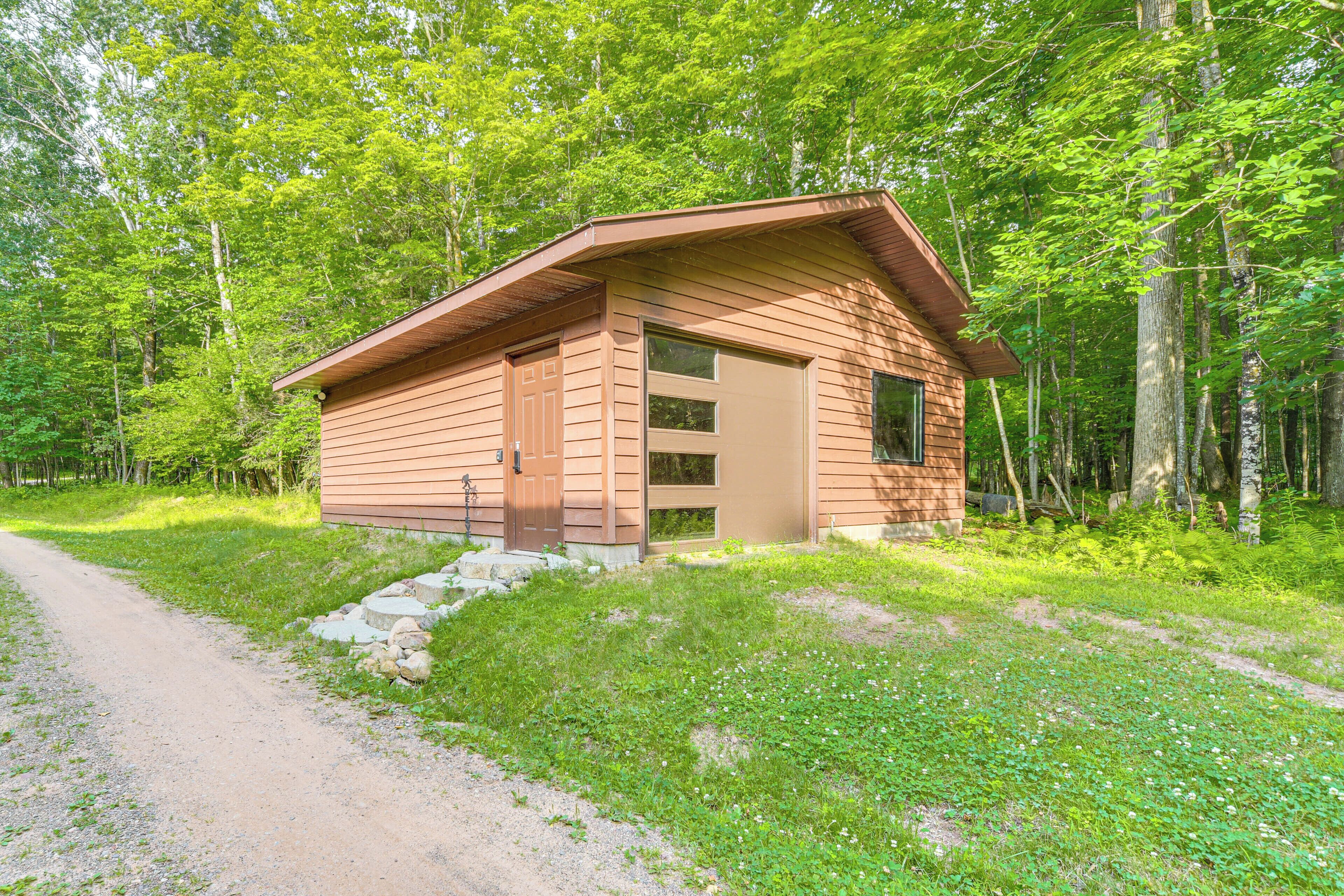 A small cabin with a sloped roof, a front door, and a window. It is surrounded by a forested area with a dirt path leading to it.