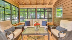 Un rincón interior acogedor con muebles de mimbre y una mesa de centro de vidrio, con ventanas amplias que ofrecen vistas al exterior.