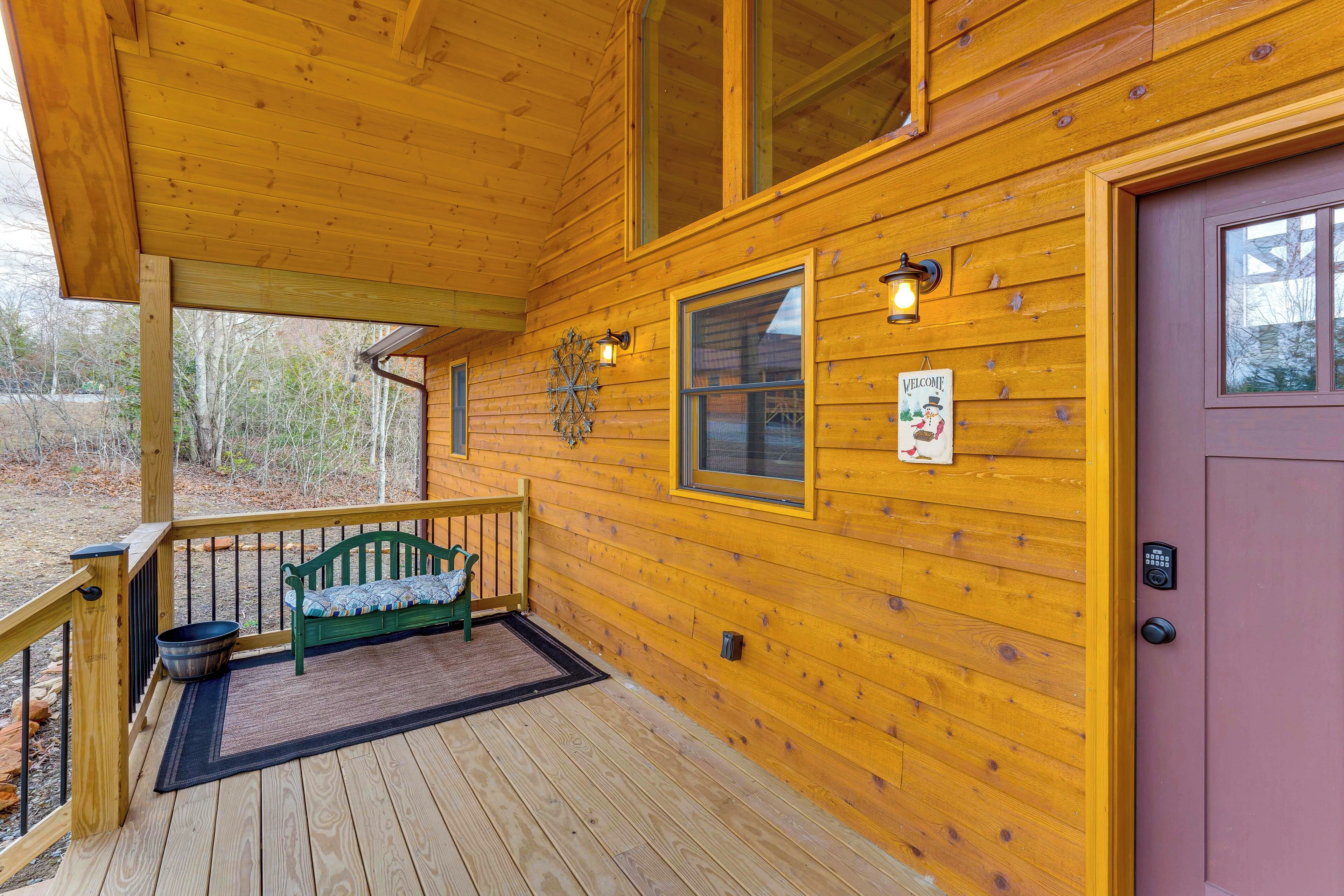 A wooden cabin with a porch, a green bench, and a welcome sign.