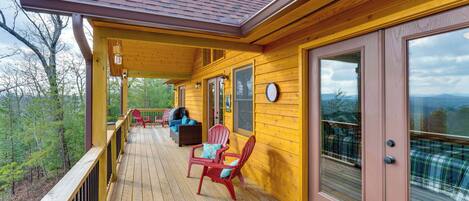 A wooden deck with outdoor seating and a view of the surrounding forest.