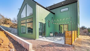Un edificio moderno con grandes ventanales, un patio con mobiliario exterior e iluminación con guirnaldas.