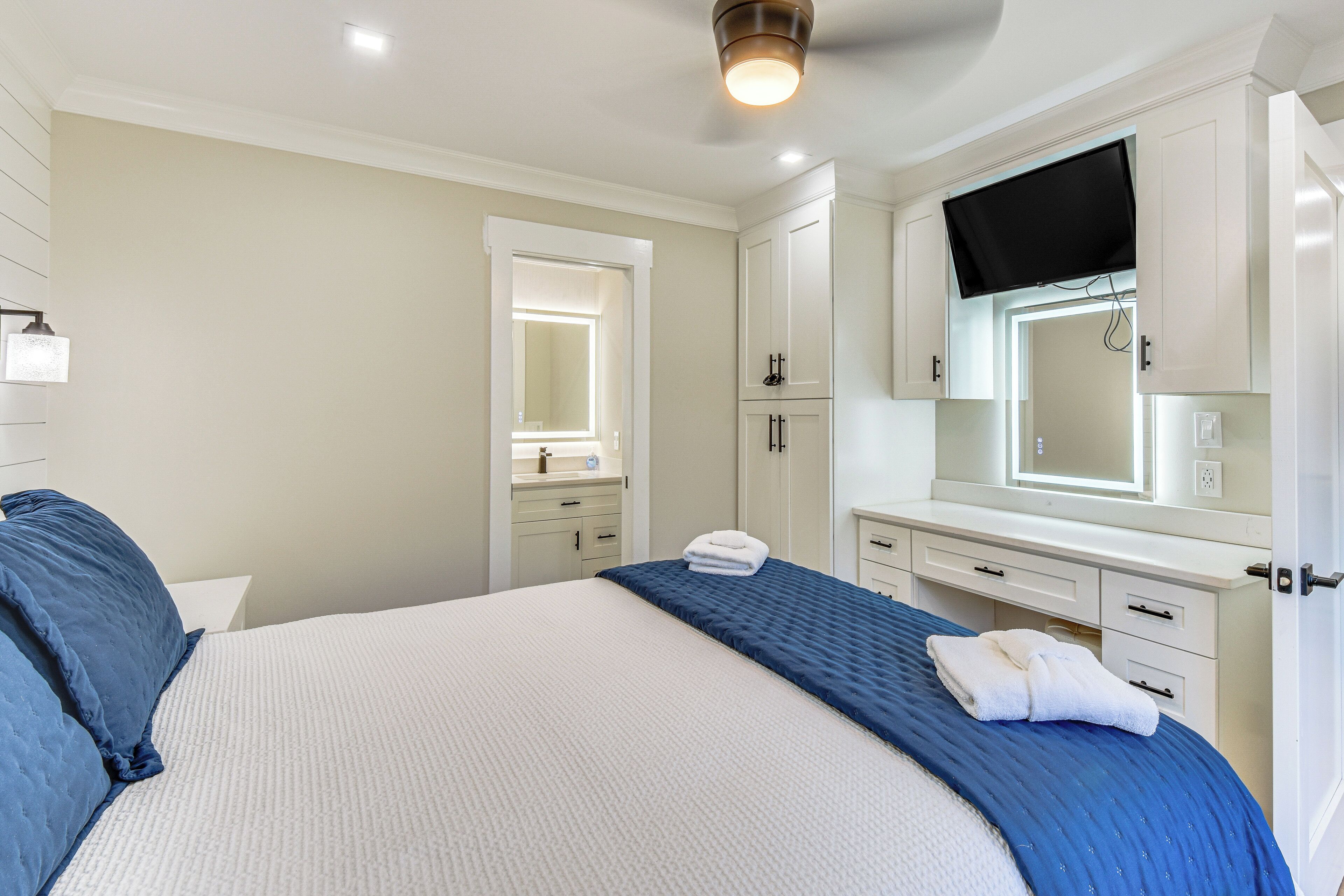 Un dormitorio con una cama grande, una mesita de noche, un espejo y un televisor montado en la pared.
