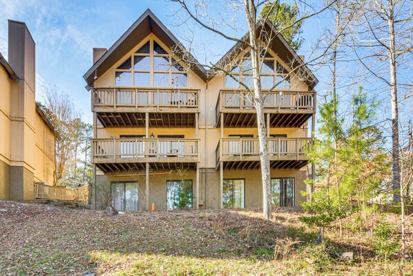 A multi-story wooden building with balconies, large windows, and a landscaped area with trees.