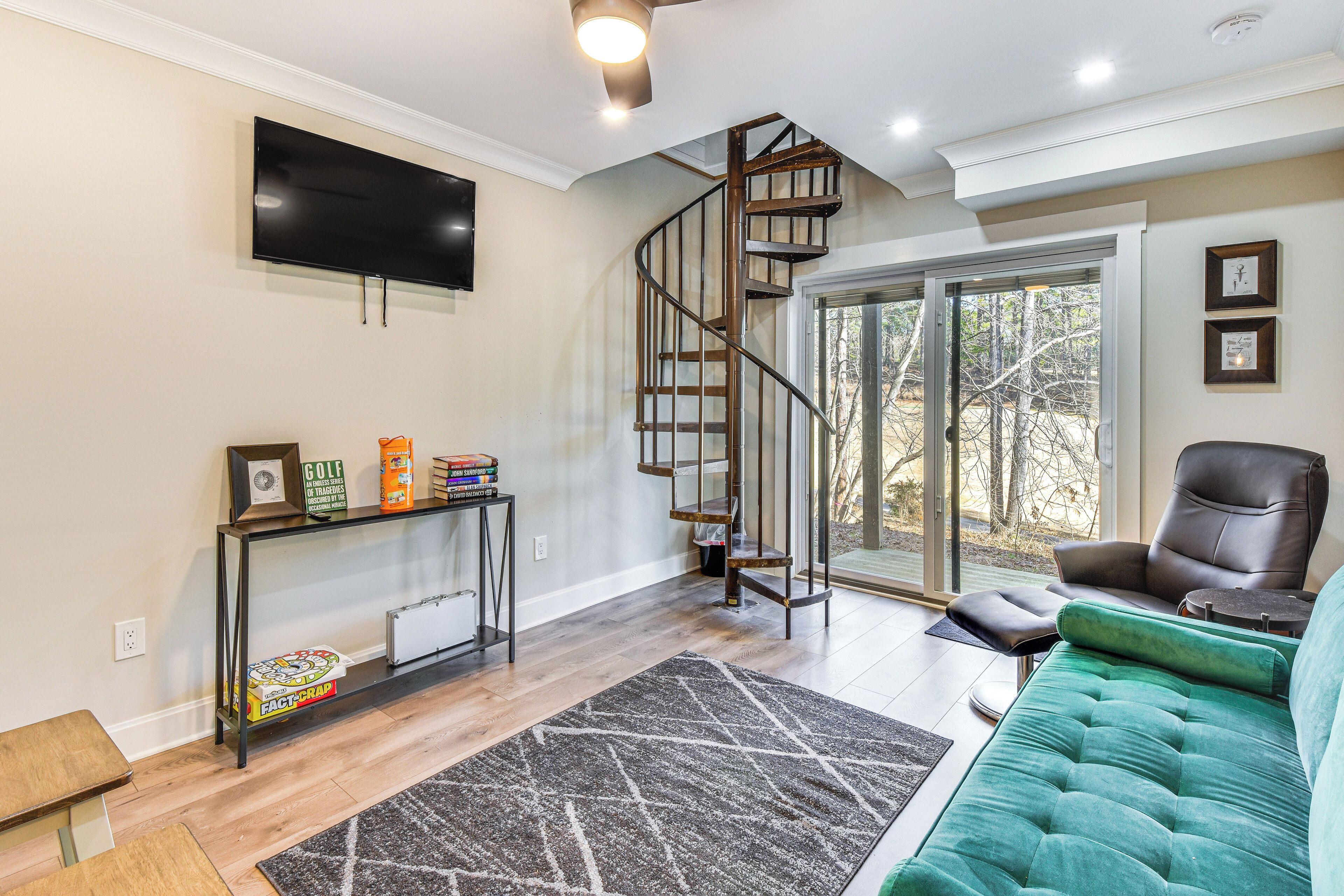 A living room with a spiral staircase, a TV mounted on the wall, a green sofa, and a coffee table.