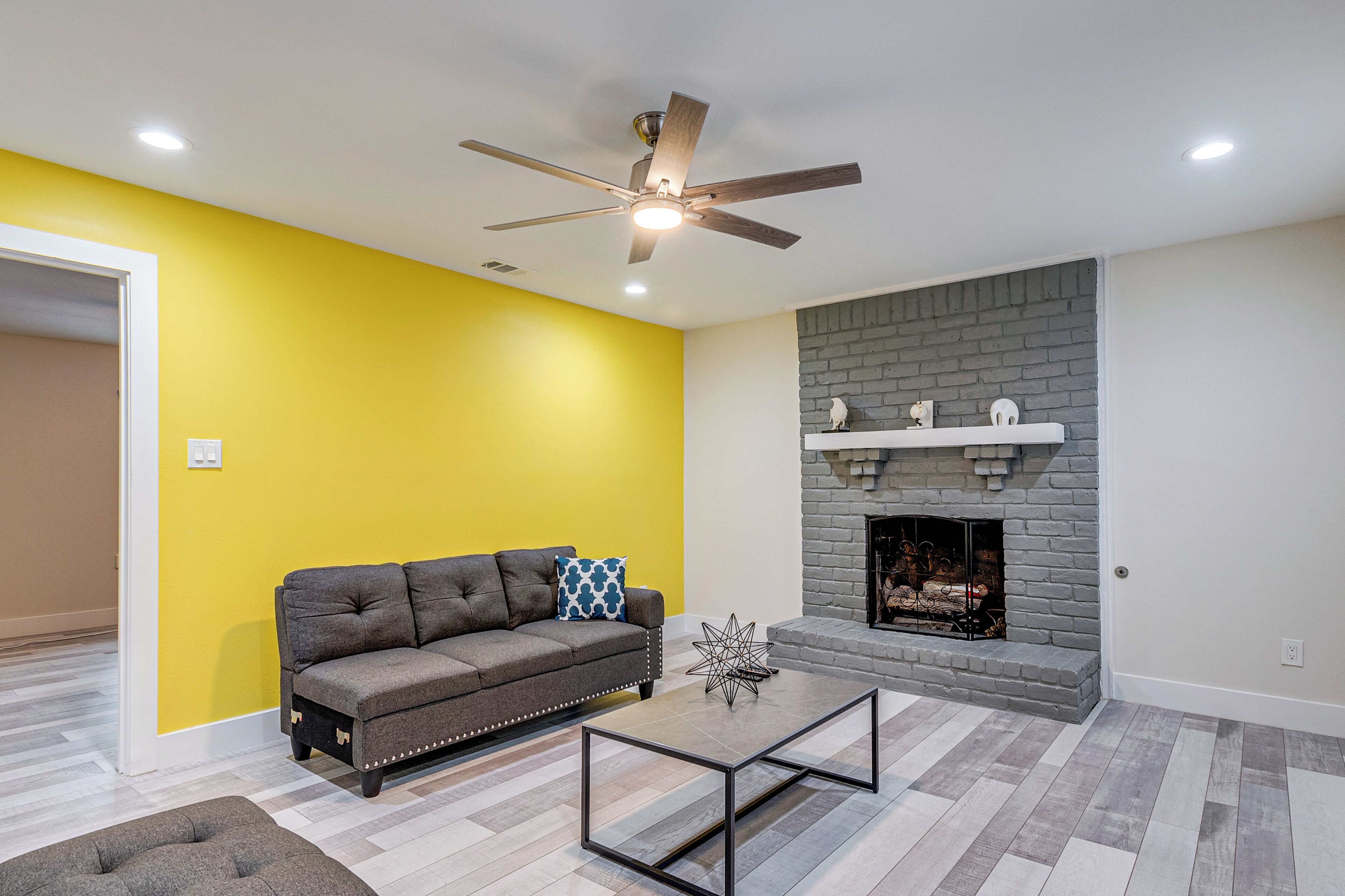 A living room with a gray sofa, a coffee table, a fireplace, and a ceiling fan.