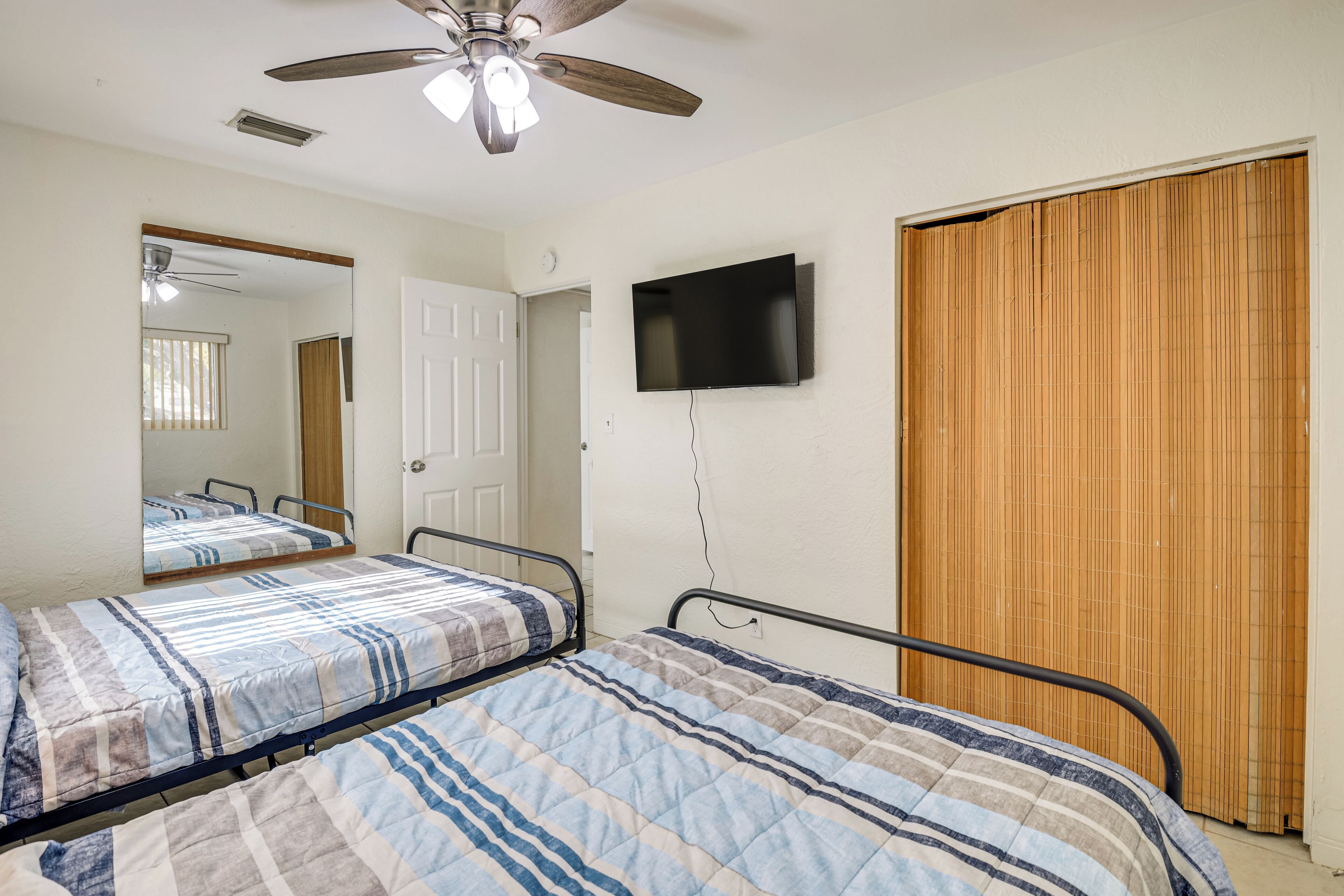 A bedroom with two beds, a ceiling fan, a television, and a sliding door.