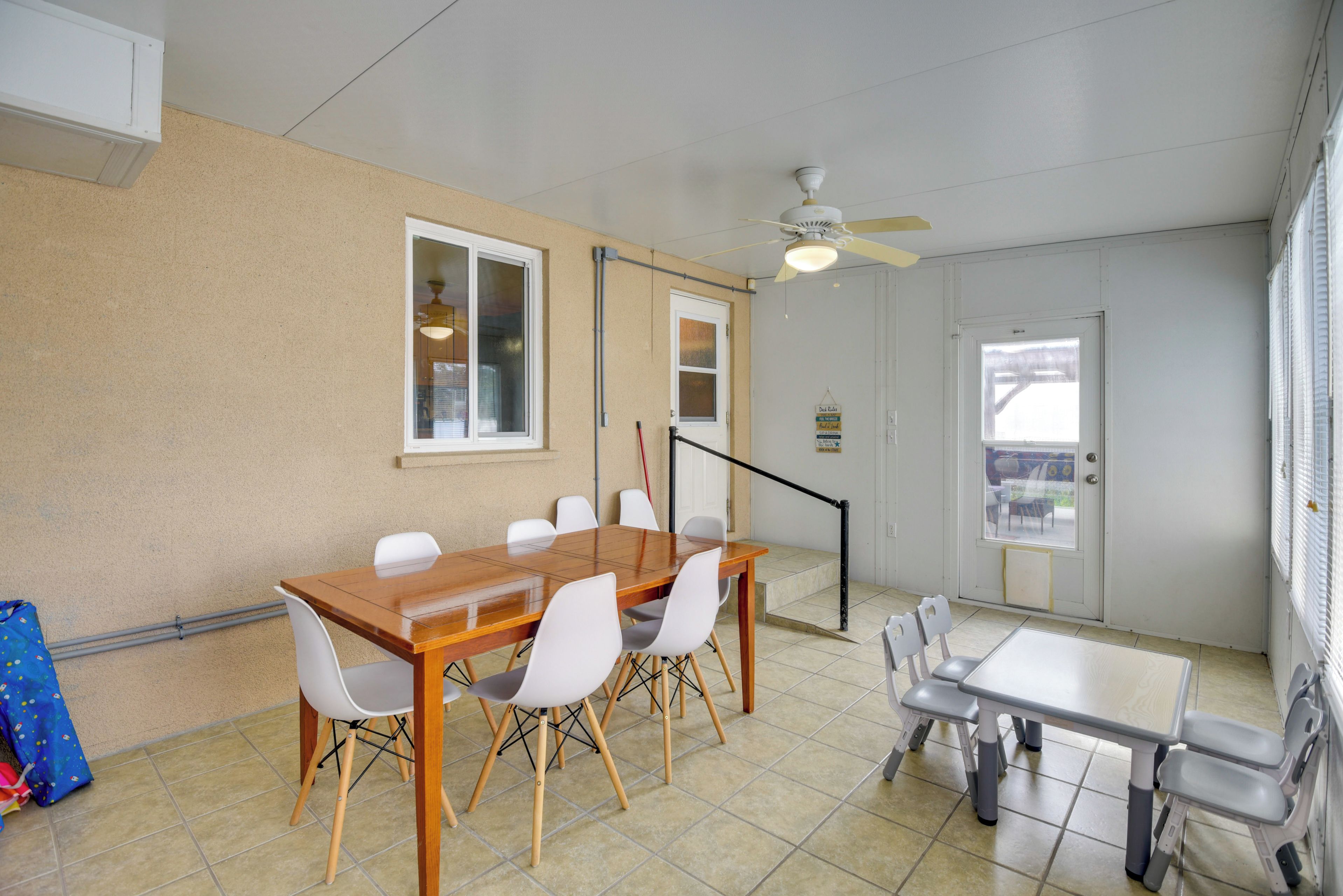 A dining area with a wooden table and chairs, a ceiling fan, and a view of the outdoors through a door.
