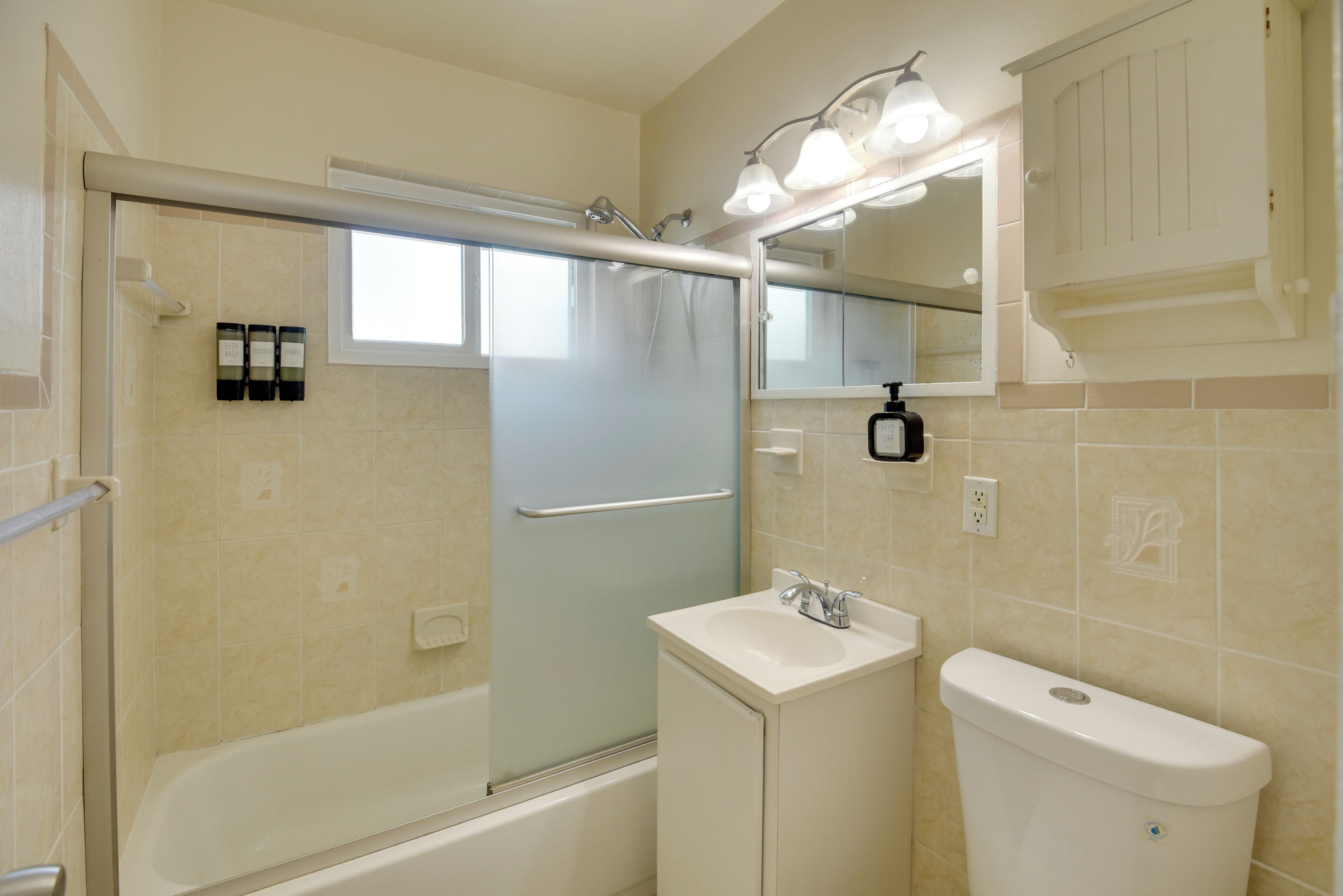 A bathroom with a bathtub, a sink, and a toilet. There is a shower curtain, a hand soap dispenser, and a mirror above the sink.