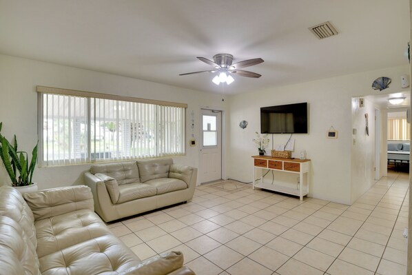 A living room with a beige sofa, a TV mounted on the wall, and a ceiling fan.