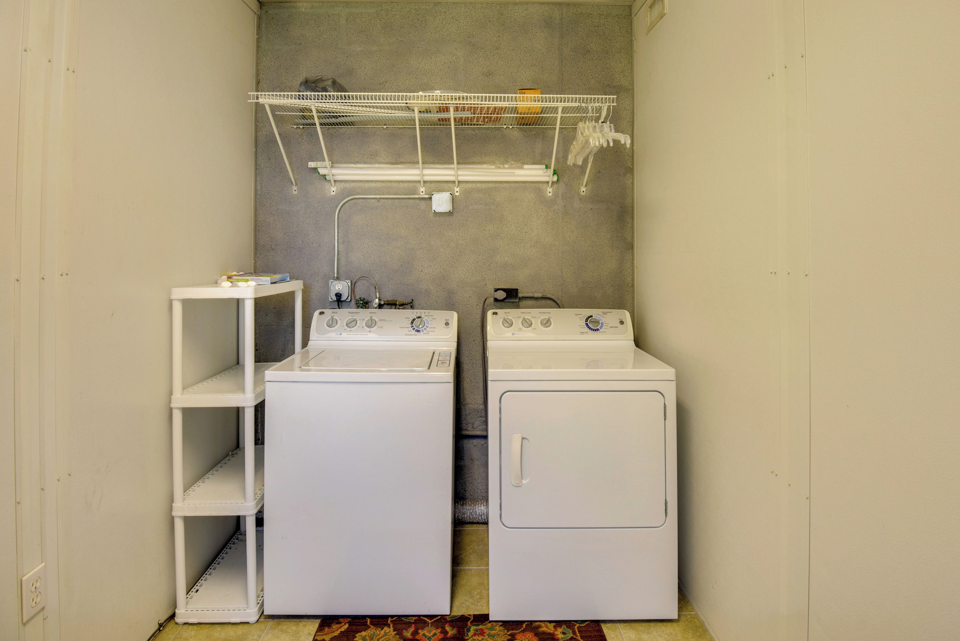 Een wasserette met twee gestapelde wasmachines en drogers, een droogrek erboven en een klein tafeltje met spullen erop.