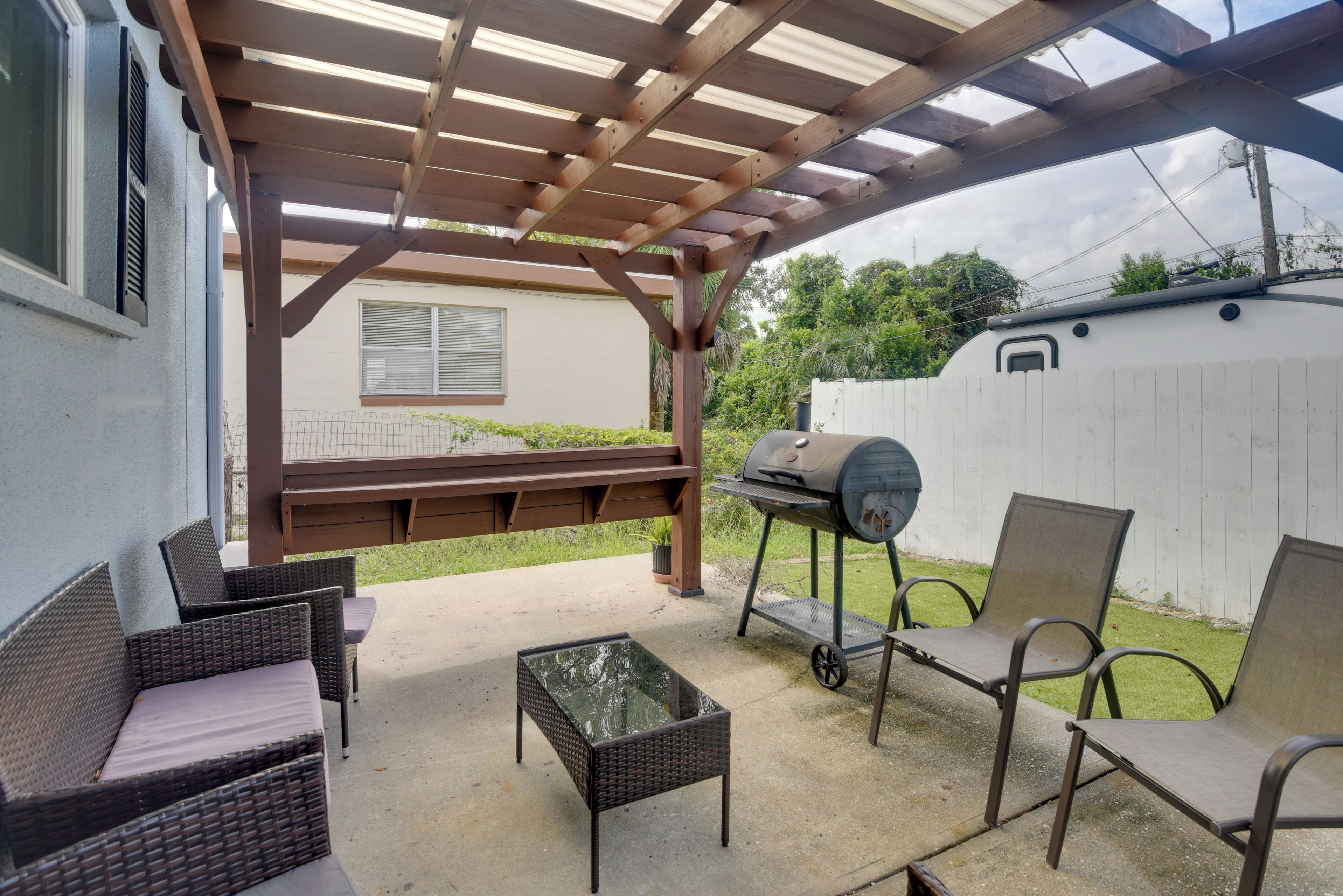 Une terrasse extérieure dotée d’une pergola, d’un barbecue, de meubles en osier et d’une clôture blanche.
