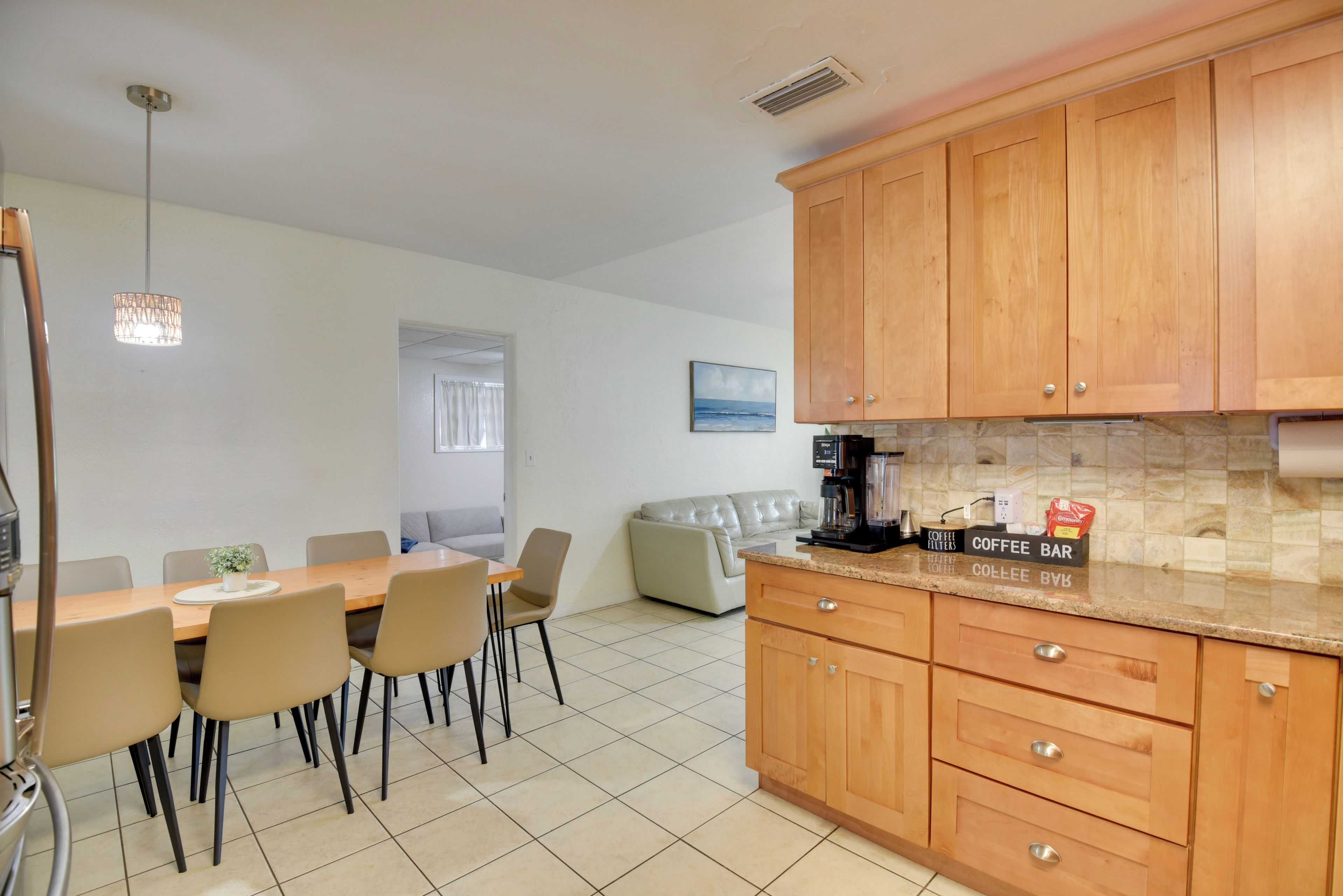 A modern kitchen with wooden cabinets, a coffee bar, and a dining area with a table and chairs.