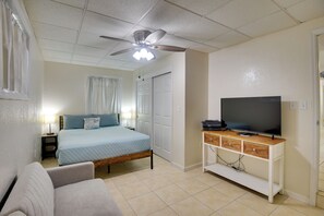 A bedroom with a bed, a TV on a wooden stand, a ceiling fan, and a door.
