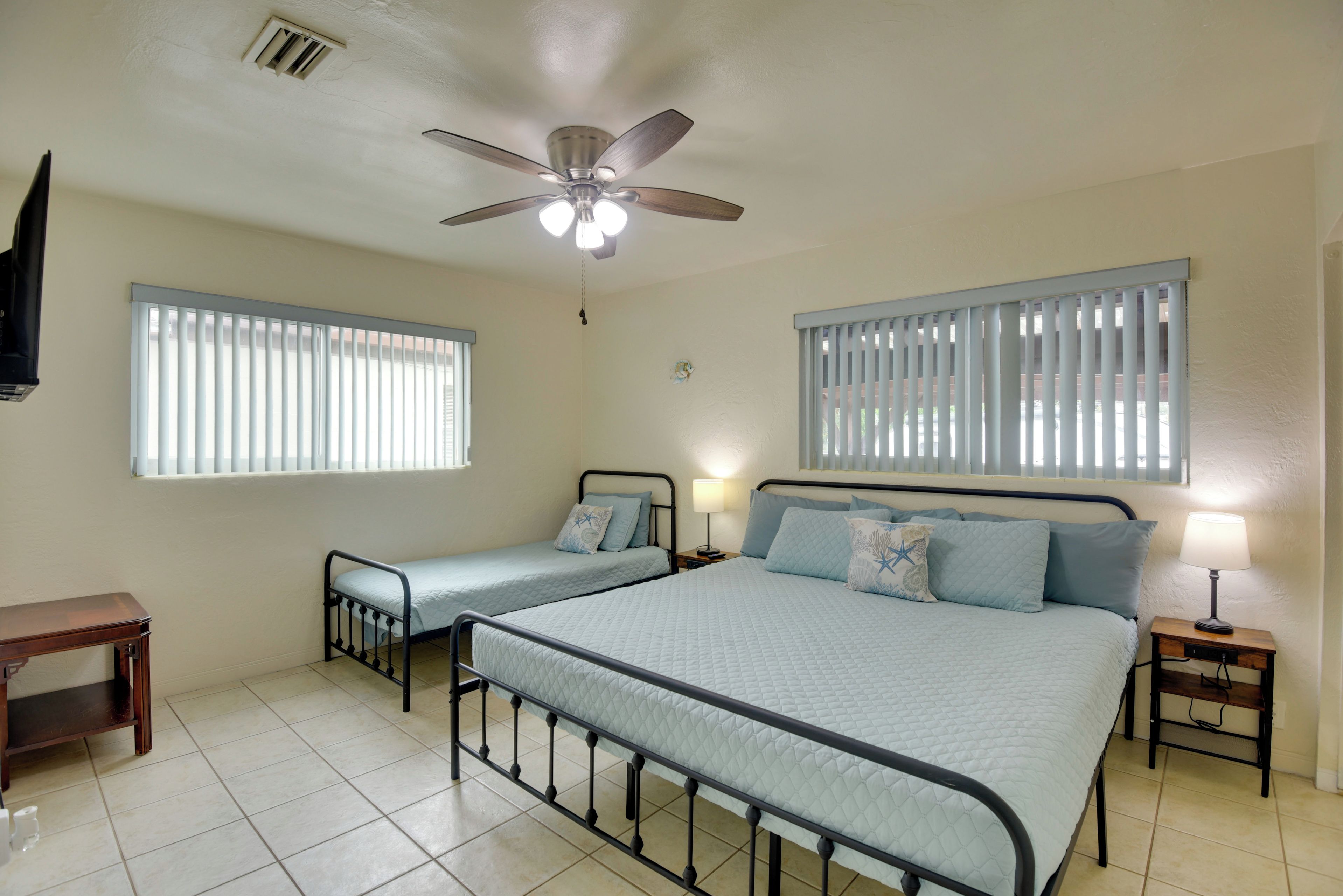 A bedroom with two single beds, a ceiling fan, and windows with blinds.
