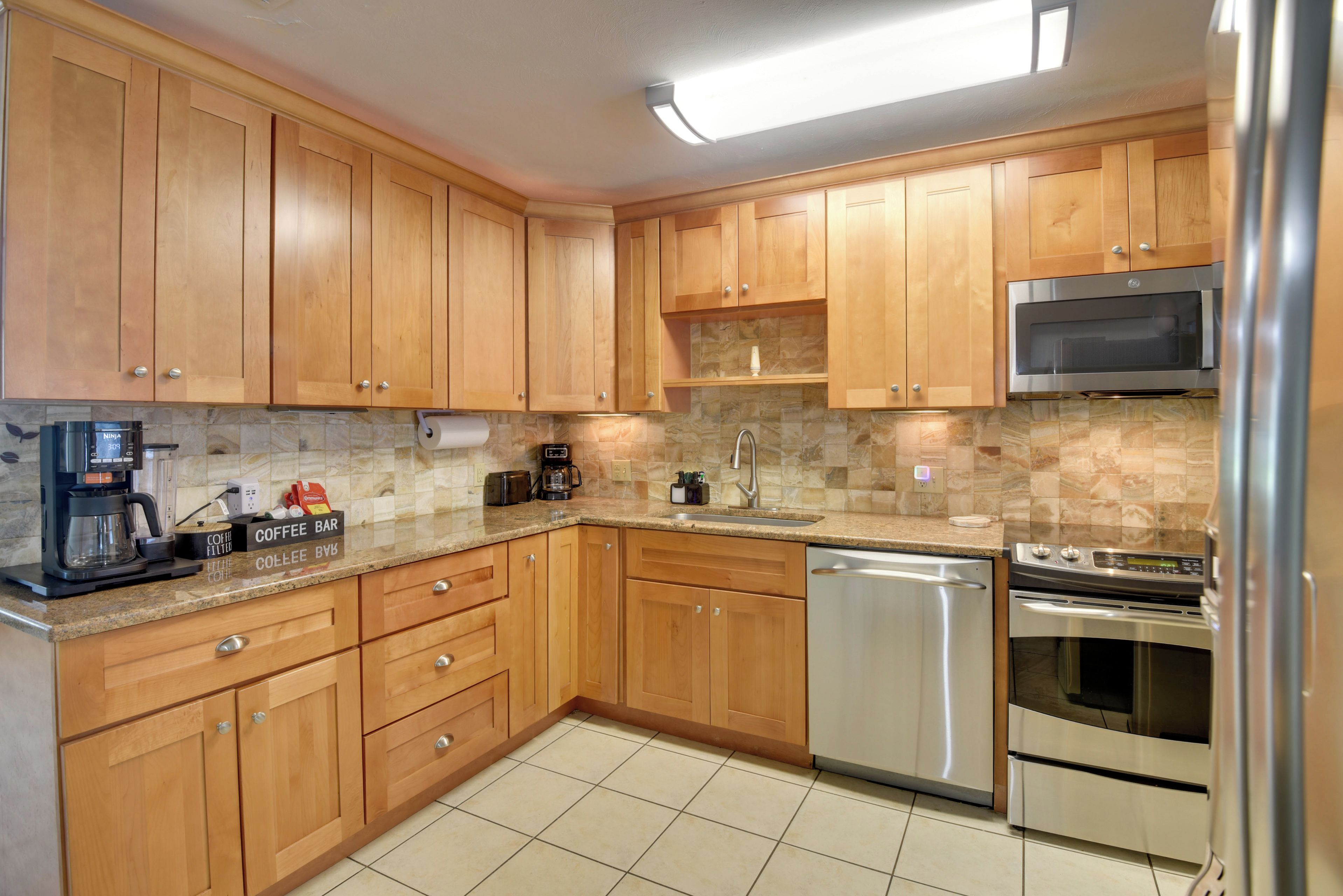 A kitchen with wooden cabinets, a stainless steel refrigerator, a microwave, a coffee maker, and a dishwasher.