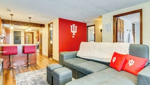 Een moderne woonkamer met een grijze hoekbank, rode kussens en een rode wand met een logo.