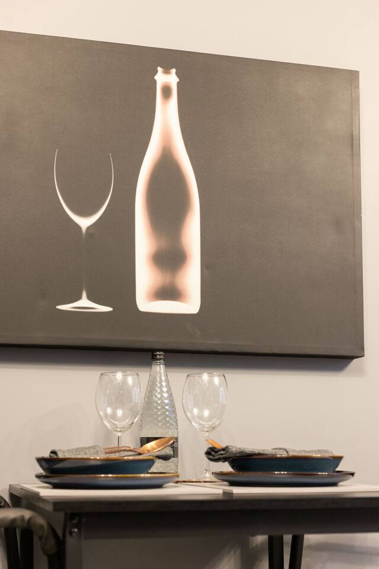 Een eettafel met een wijnglas en een fles, een kleine kroonluchter en een bord met een lepel.