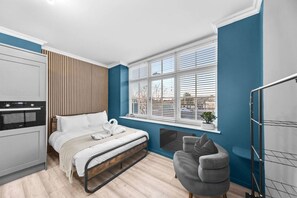 Una camera da letto moderna con un letto, un forno a incasso, una finestra con persiane e una poltrona grigia.