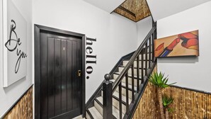 Un intérieur moderne avec une porte noire, un escalier aux finitions en bois et un tableau accroché au mur.