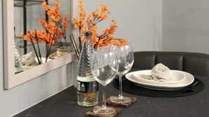 Une cuisine moderne avec un plan de travail noir, deux verres à vin, une bouteille de vin et des fleurs décoratives de couleur orange.