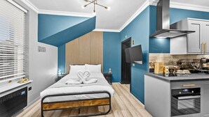 Una habitación de hotel moderna con una cama, una pequeña kitchenette, un televisor y una pared de listones de madera.