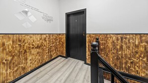 Un pasillo con pared de paneles de madera, una puerta negra y una escalera con barandal negro.