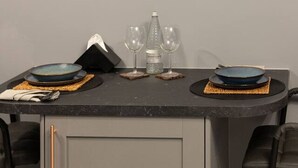 Un comedor con una mesa dispuesta para dos personas, con dos platos azules, una botella y dos vasos. Hay dos obras de arte enmarcadas en la pared sobre la mesa.