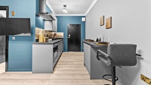 Una cocina compacta con una isla central, horno empotrado y estufa. Se observa una puerta oscura al fondo y una barra con taburetes.
