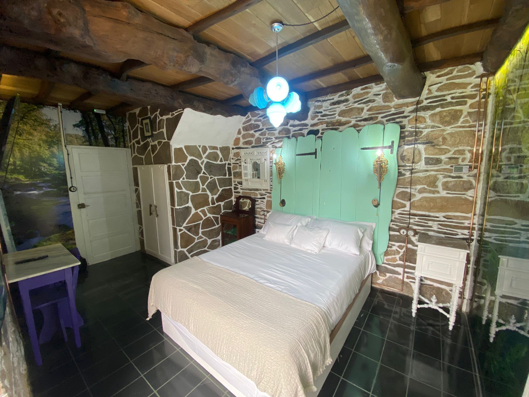 Un dormitorio con pared de piedra, una cama, un armario y una pequeña mesa.