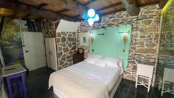 Un dormitorio con pared de piedra, una cama, un armario y una pequeña mesa.