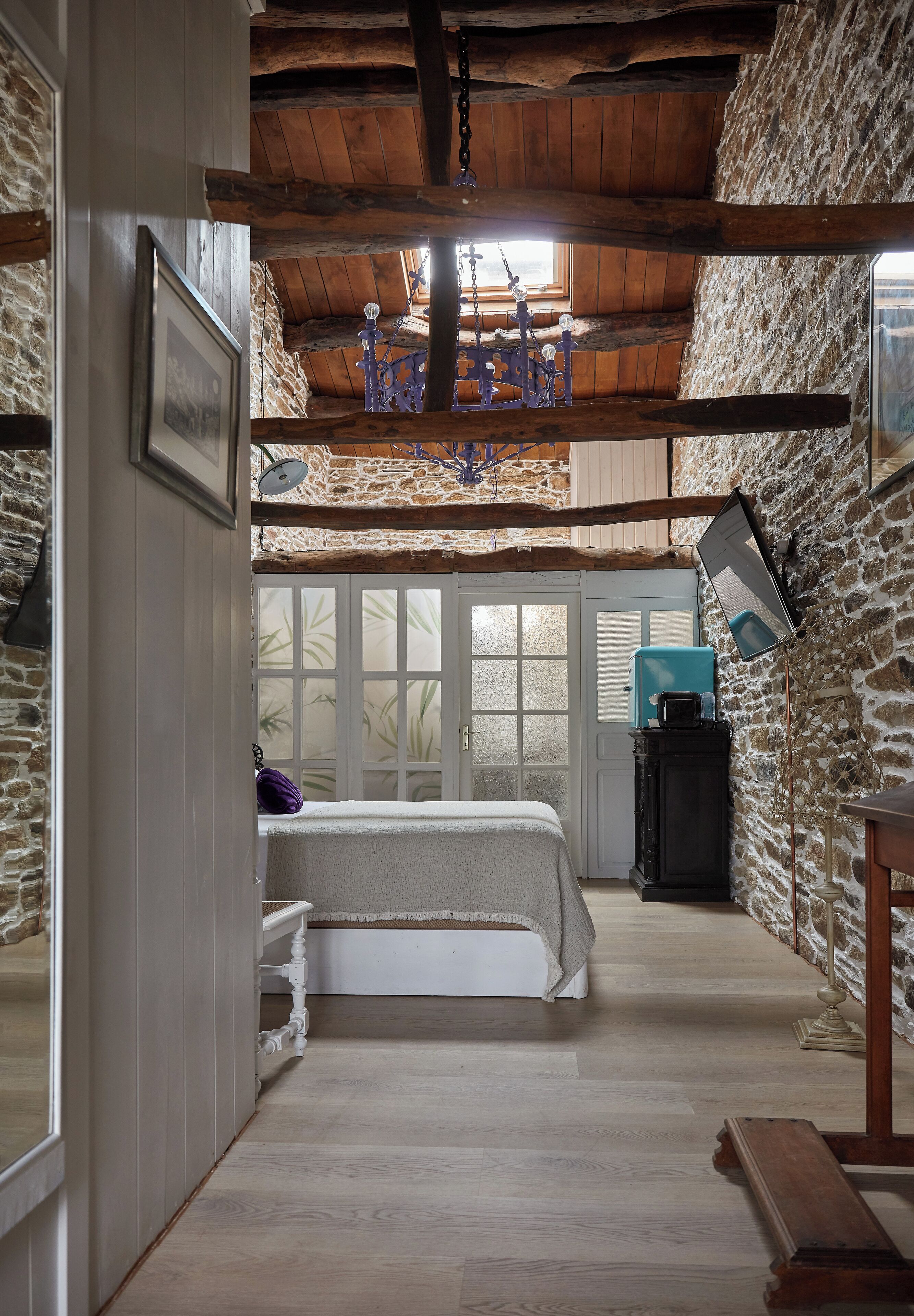 Una habitación rústica con vigas de madera a la vista, una pared de piedra, una cama, un escritorio y una ventana con vistas.