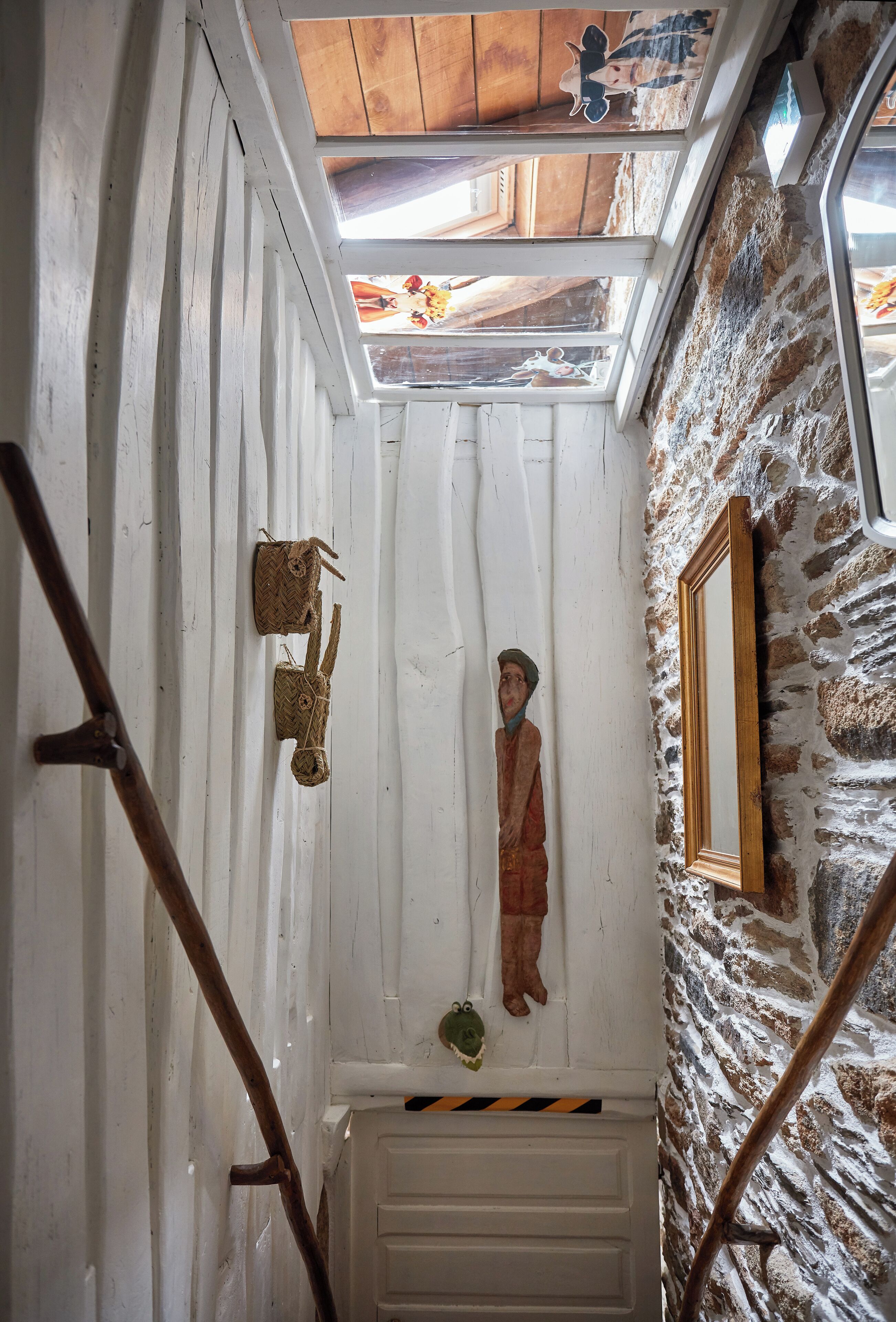 Un escalier étroit avec des rampes en bois, un mur en pierre et un plafond en bois doté de lucarnes.