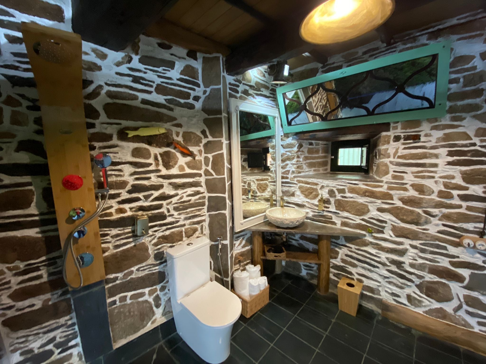 Un baño con pared de piedra, tocador de madera, inodoro y lavamanos.