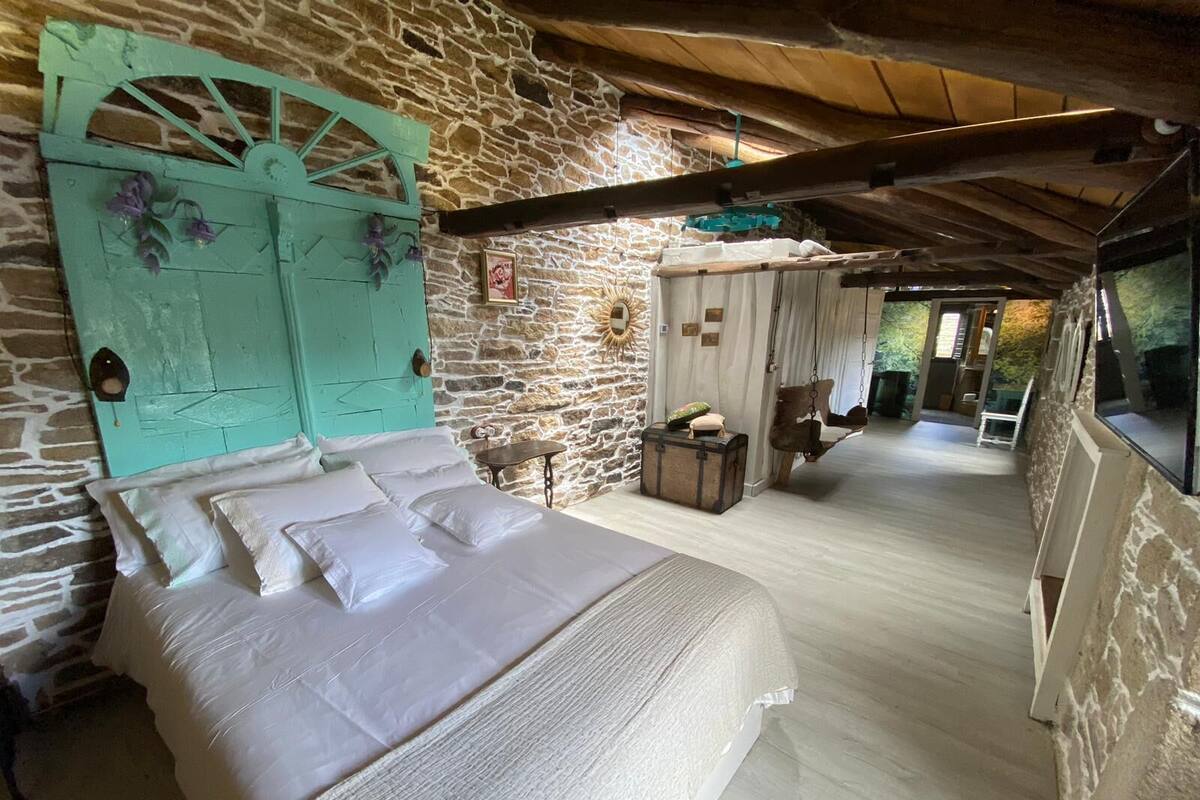 A bedroom with a large bed, stone walls, and a rustic wooden ceiling.