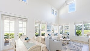 Un salon spacieux avec une grande table à manger, des sièges confortables et de grandes fenêtres offrant une vue sur l’extérieur.