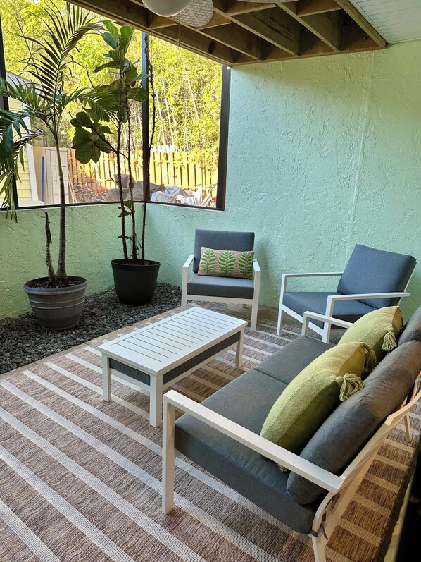 A patio area with a white table and two chairs, a sofa with cushions, and potted plants.